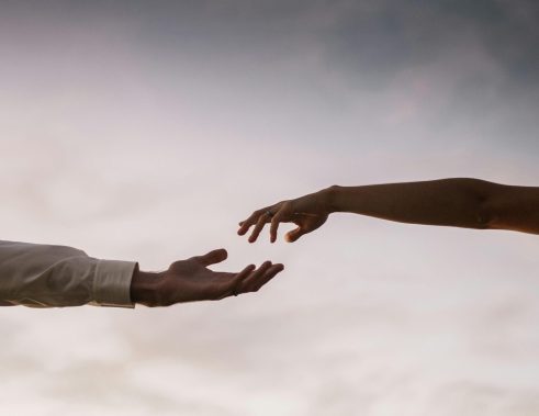 Two hands reaching towards each other against a soft twilight sky symbolizing connection and love.